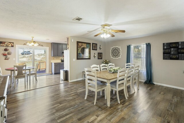 dining space with ceiling fan with notable chandelier, dark wood finished floors, visible vents, and baseboards