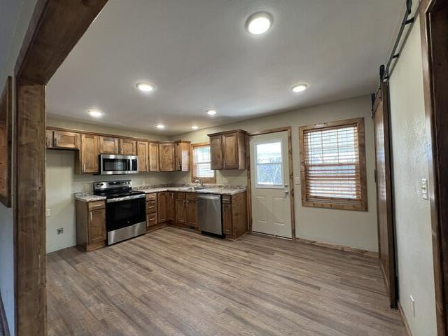 kitchen with a barn door, appliances with stainless steel finishes, sink, and light hardwood / wood-style flooring