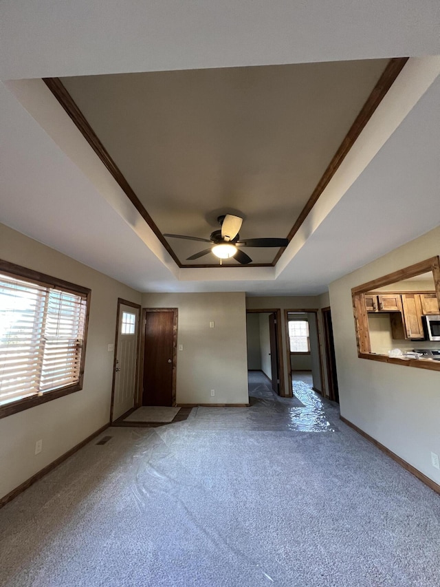 unfurnished living room featuring a tray ceiling, carpet floors, and ceiling fan