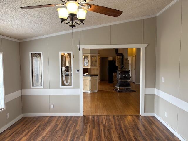 spare room featuring ceiling fan, ornamental molding, a textured ceiling, dark hardwood / wood-style flooring, and a wood stove