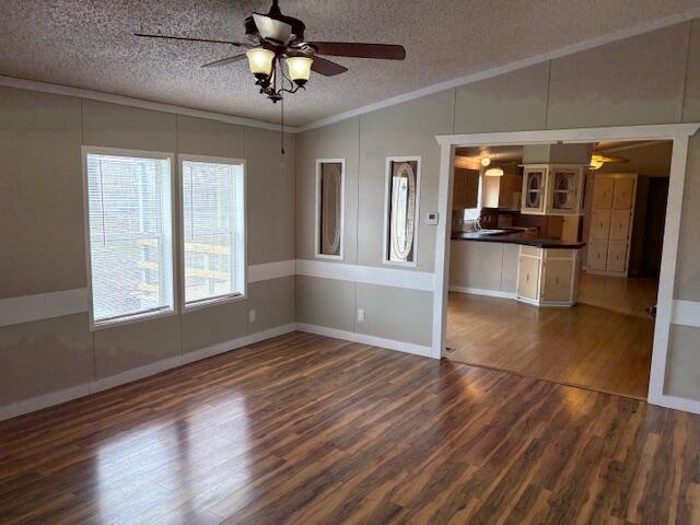 spare room featuring lofted ceiling, crown molding, dark wood-type flooring, ceiling fan, and a textured ceiling