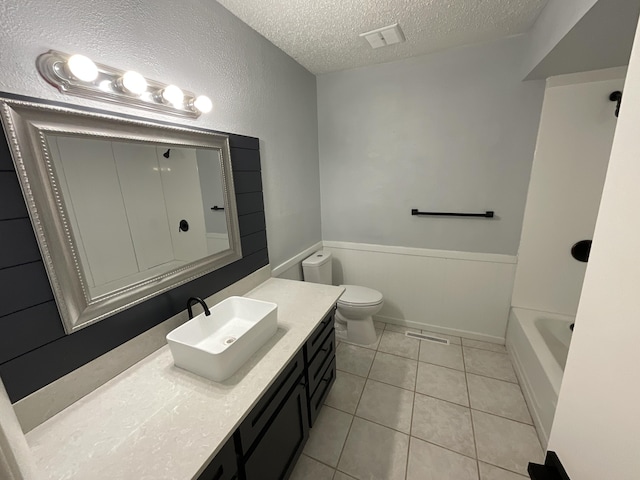 bathroom with tile patterned floors, toilet, a textured ceiling, vanity, and a washtub