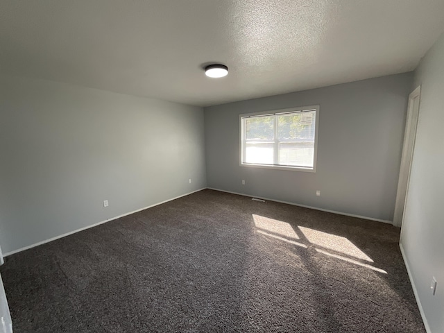 unfurnished room with dark carpet and a textured ceiling