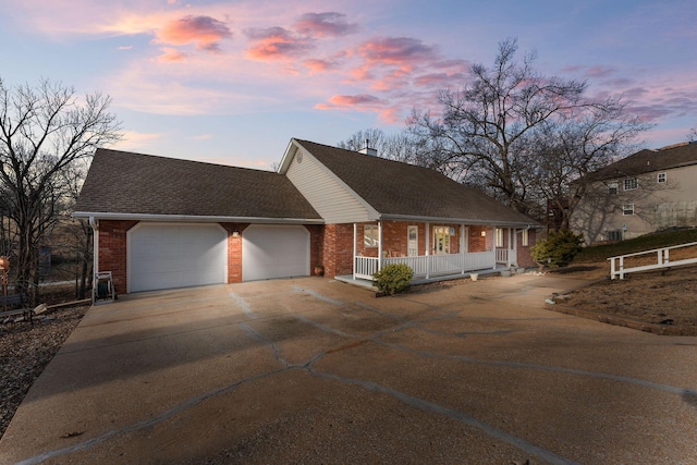 view of front of house with a garage, concrete driveway, roof with shingles, covered porch, and brick siding