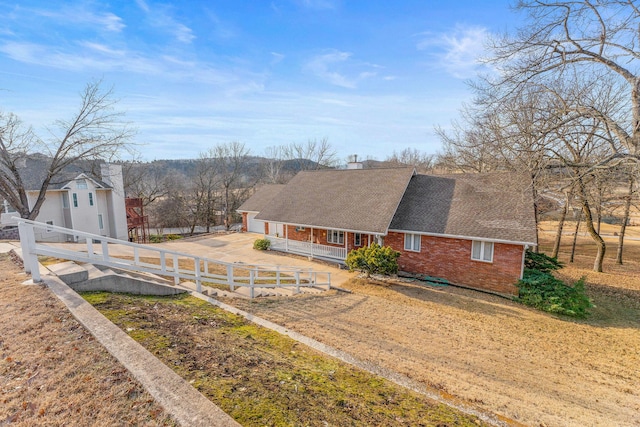 view of front of home with brick siding, roof with shingles, a porch, and fence