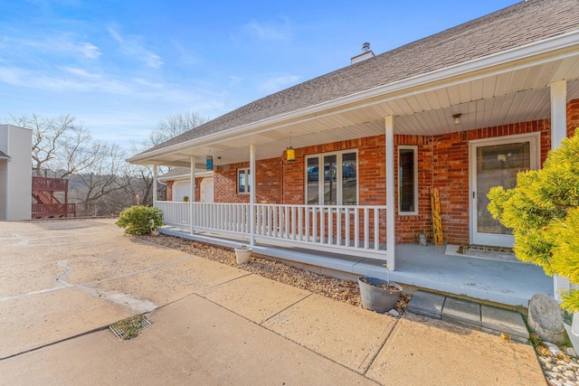 exterior space with covered porch, roof with shingles, and brick siding