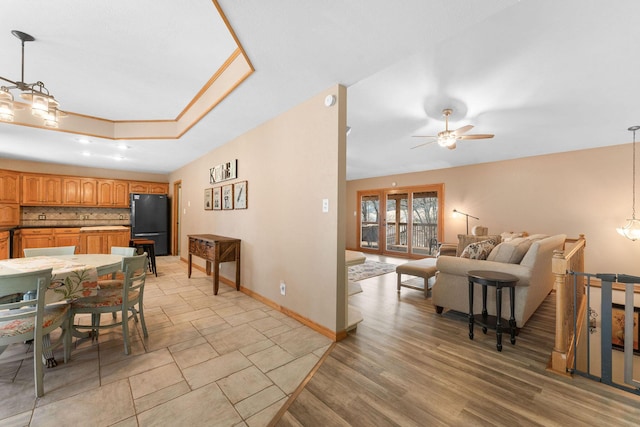 dining room with light wood-type flooring, a raised ceiling, baseboards, and ceiling fan with notable chandelier