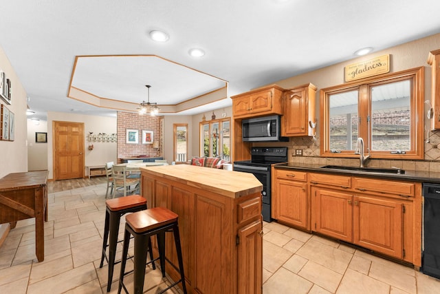 kitchen with a kitchen island, wood counters, a tray ceiling, black appliances, and a sink