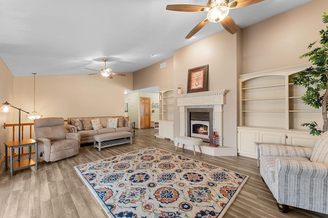 living area with built in features, a ceiling fan, a glass covered fireplace, wood finished floors, and high vaulted ceiling