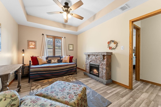 living room with light wood-type flooring, a tray ceiling, visible vents, and a fireplace