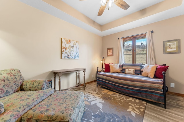 sitting room with light wood-type flooring, baseboards, a raised ceiling, and a ceiling fan