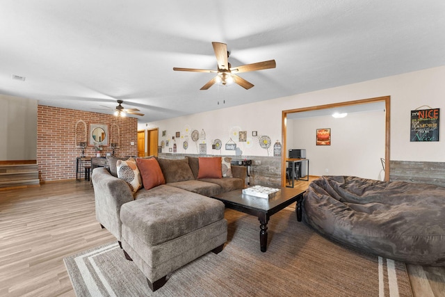 living area with brick wall, light wood-type flooring, visible vents, and a ceiling fan