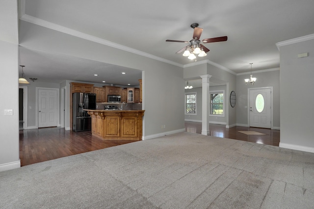 unfurnished living room featuring dark carpet, ornamental molding, decorative columns, and ceiling fan with notable chandelier