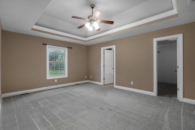 unfurnished bedroom featuring ceiling fan, a walk in closet, a tray ceiling, and carpet