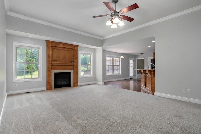 unfurnished living room featuring crown molding, ceiling fan, a tile fireplace, and light carpet