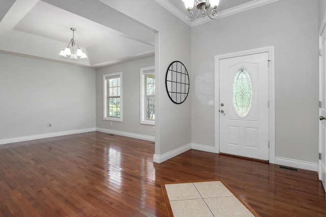 foyer entrance featuring an inviting chandelier, dark hardwood / wood-style floors, a raised ceiling, and crown molding