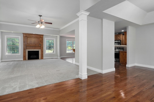 unfurnished living room with dark wood-type flooring, a large fireplace, ornamental molding, ceiling fan, and decorative columns