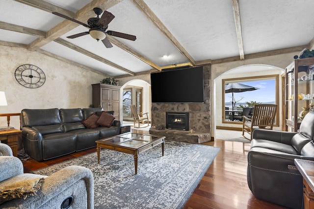 living room with vaulted ceiling with beams, a textured ceiling, dark hardwood / wood-style floors, ceiling fan, and a fireplace