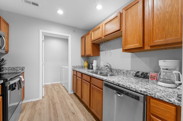 kitchen featuring sink, washing machine and dryer, appliances with stainless steel finishes, light stone countertops, and light hardwood / wood-style floors