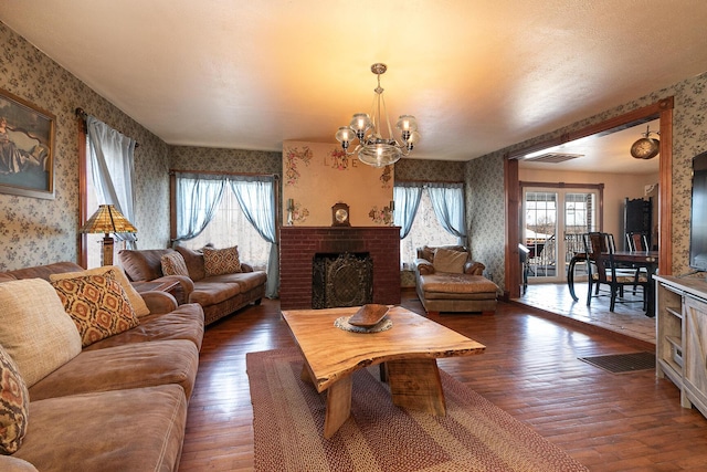 living room featuring an inviting chandelier, dark hardwood / wood-style flooring, and a brick fireplace