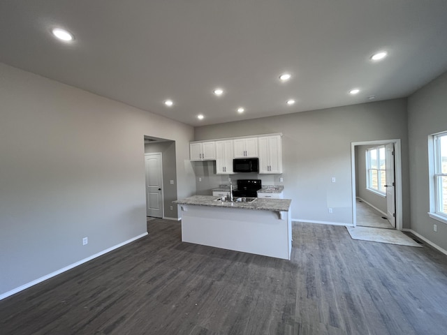 kitchen with dark hardwood / wood-style floors, electric range oven, white cabinetry, a kitchen island with sink, and light stone counters