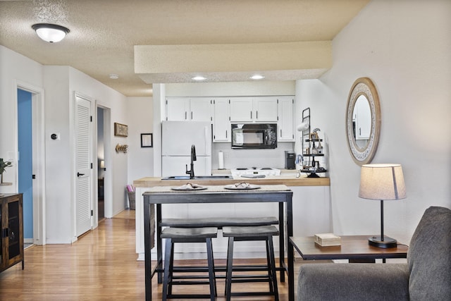 kitchen with sink, light wood-type flooring, kitchen peninsula, white fridge, and white cabinets