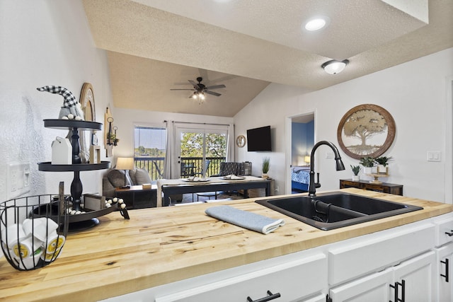 kitchen featuring sink, ceiling fan, white cabinetry, wood counters, and vaulted ceiling