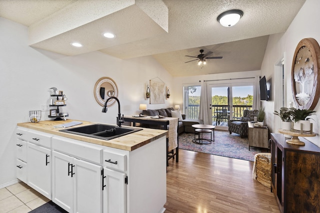 kitchen with lofted ceiling, sink, butcher block countertops, white cabinetry, and ceiling fan