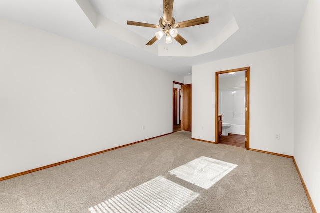 unfurnished bedroom featuring light colored carpet, a raised ceiling, and ensuite bathroom