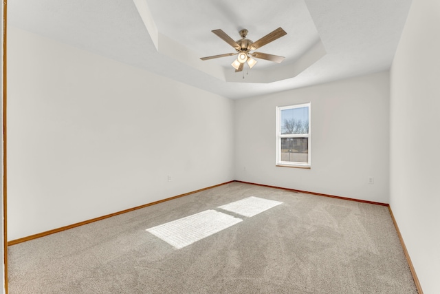 carpeted spare room with ceiling fan and a raised ceiling