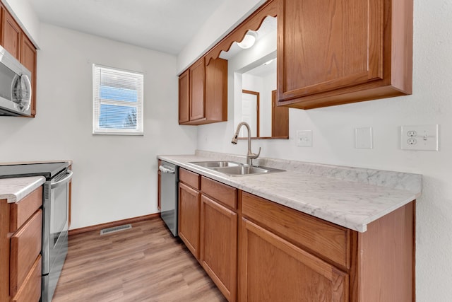 kitchen with stainless steel appliances, sink, and light hardwood / wood-style flooring