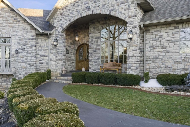 entrance to property featuring a lawn and a shingled roof