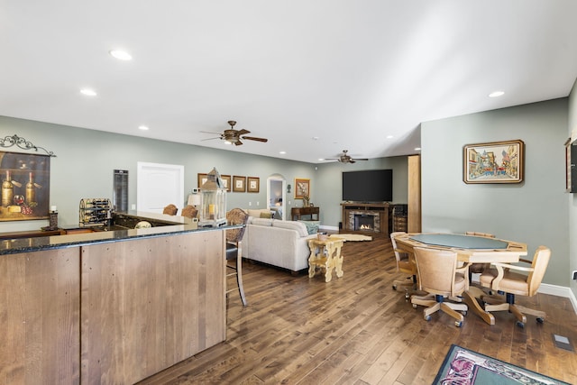 living area with a ceiling fan, dark wood-style floors, recessed lighting, a lit fireplace, and baseboards