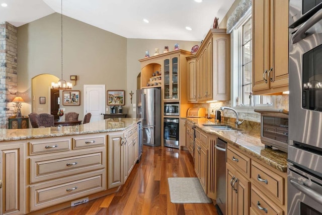 kitchen featuring sink, light stone counters, decorative light fixtures, vaulted ceiling, and stainless steel appliances