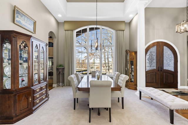 dining room with light carpet, french doors, arched walkways, a high ceiling, and an inviting chandelier