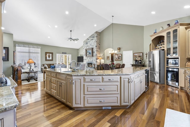 kitchen with glass insert cabinets, open floor plan, a center island with sink, a fireplace, and stainless steel appliances