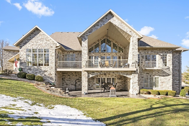 back of house featuring a lawn, a shingled roof, a balcony, and a patio area