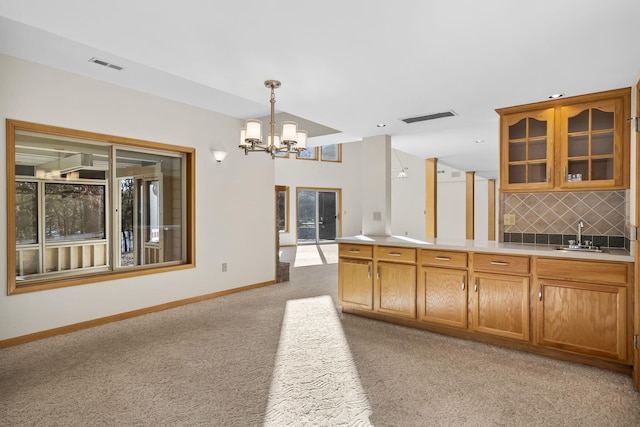 kitchen featuring pendant lighting, sink, backsplash, a chandelier, and light colored carpet