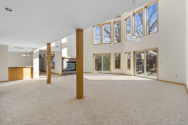 unfurnished living room with light colored carpet, a fireplace, a chandelier, and a towering ceiling