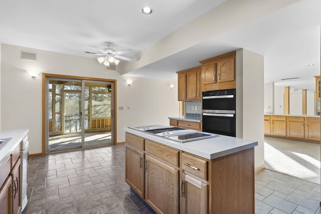 kitchen with stovetop, ceiling fan, double oven, backsplash, and a center island