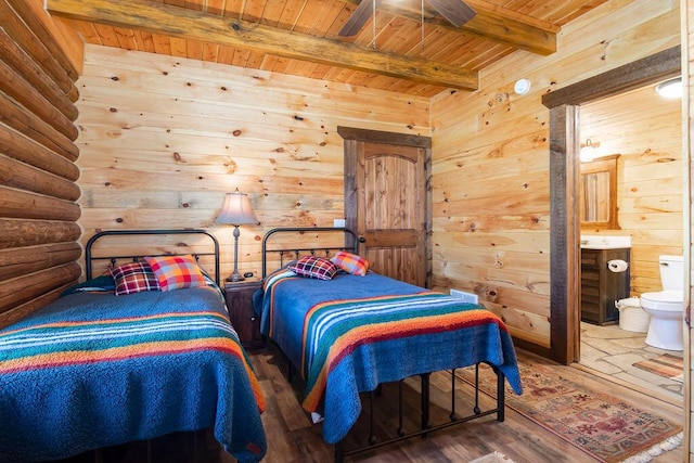 bedroom featuring beamed ceiling, log walls, hardwood / wood-style flooring, wooden ceiling, and ensuite bath