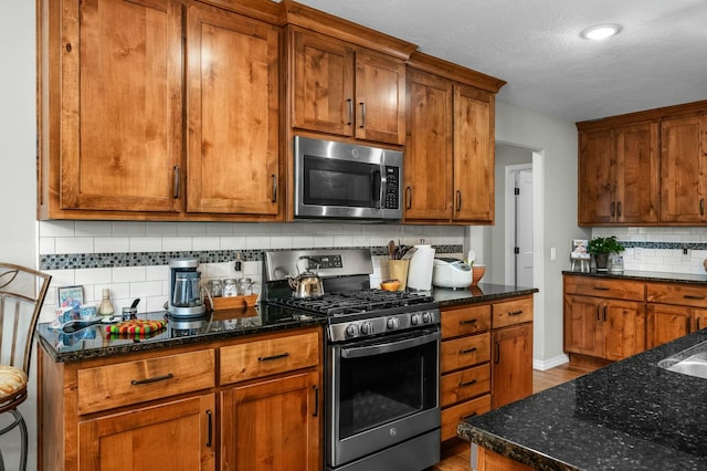 kitchen with appliances with stainless steel finishes, dark stone countertops, a textured ceiling, and decorative backsplash