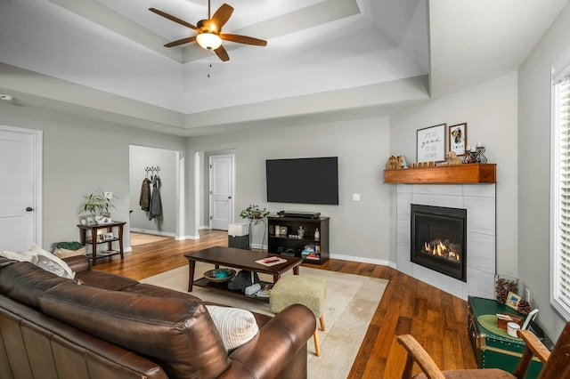 living room with hardwood / wood-style flooring, ceiling fan, a tray ceiling, and a fireplace