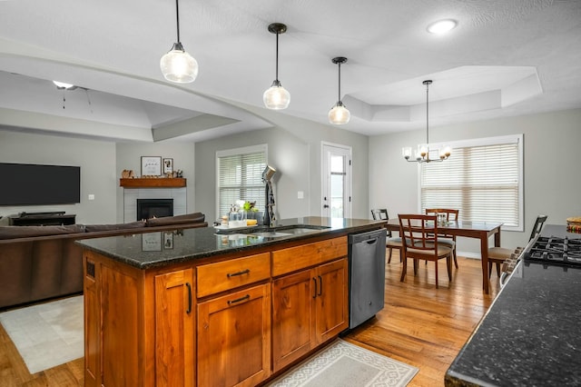 kitchen with hanging light fixtures, a kitchen island with sink, stainless steel dishwasher, and a tray ceiling