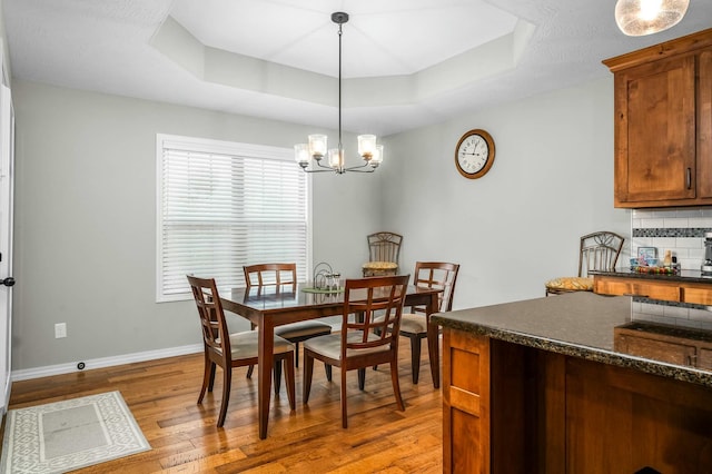 dining area with a raised ceiling, a notable chandelier, and light hardwood / wood-style floors