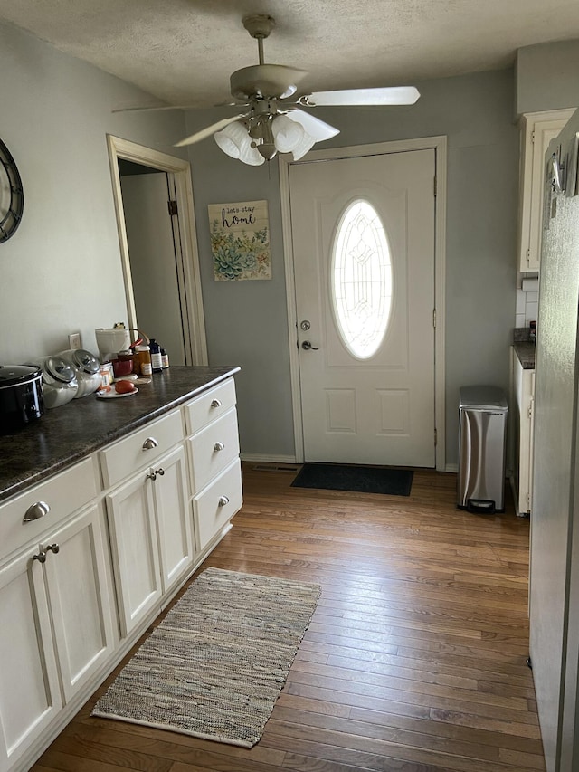 foyer entrance with a ceiling fan, dark wood-style flooring, baseboards, and a textured ceiling
