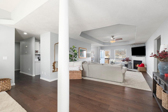 living room with dark wood-type flooring, ceiling fan, a tray ceiling, and a textured ceiling