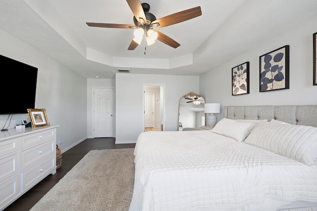 bedroom with dark hardwood / wood-style floors, connected bathroom, ceiling fan, and a tray ceiling