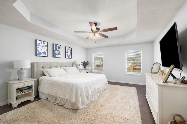 bedroom with a raised ceiling, ceiling fan, dark hardwood / wood-style floors, and a textured ceiling