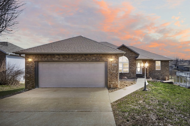 ranch-style house with driveway, roof with shingles, a garage, a lawn, and brick siding